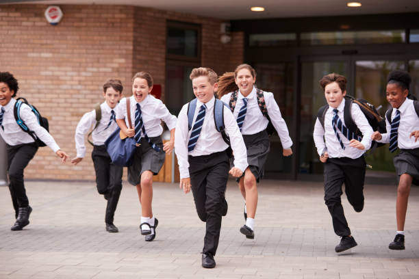 Group Of High School Students Wearing Uniform Running Out Of School Buildings Towards Camera At The End Of Class Group Of High School Students Wearing Uniform Running Out Of School Buildings Towards Camera At The End Of Class independent school education stock pictures, royalty-free photos & images