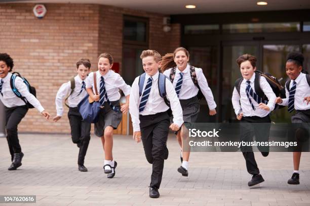 Group Of High School Students Wearing Uniform Running Out Of School Buildings Towards Camera At The End Of Class Stock Photo - Download Image Now