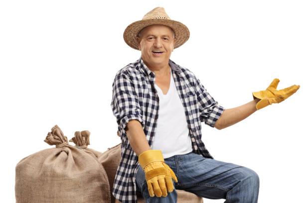 istock Old farmer sitting on burlap sacks and gesturing with his hand 1047621096