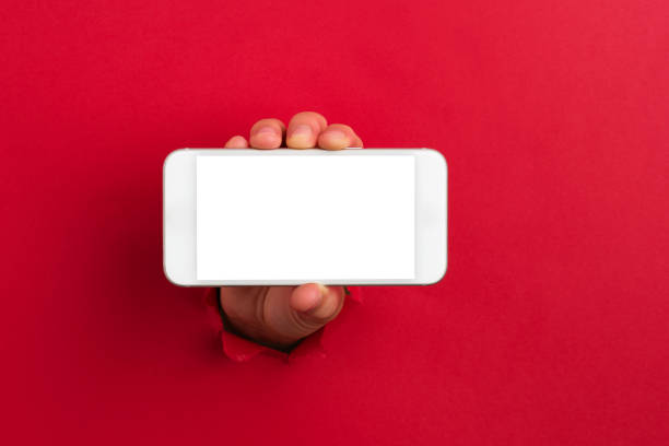 Human hand reaching through torn red paper sheet showing smart phone