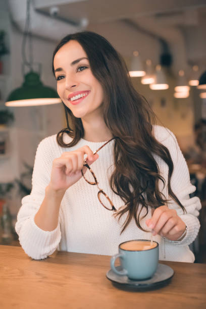 istock cheerful young woman holding eyeglasses while sitting at table with coffee cup in cafe 1047624242