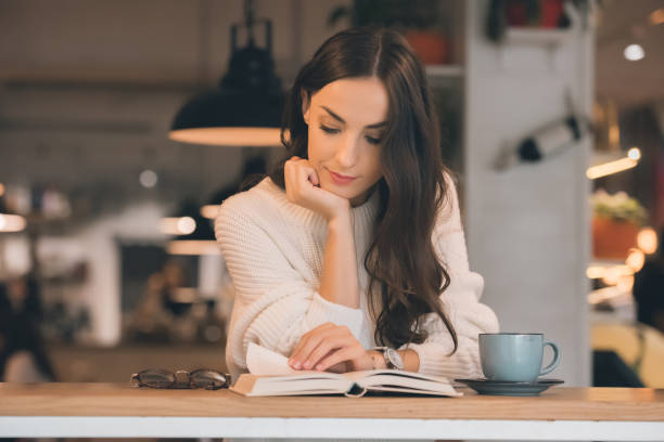 istock focused young woman reading book at table with coffee cup in cafe 1047624256