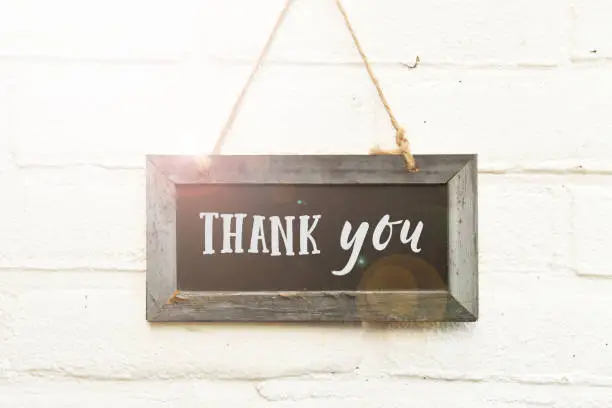 Thank you text handwritten typography on chalkboard hanging on white brick wall background