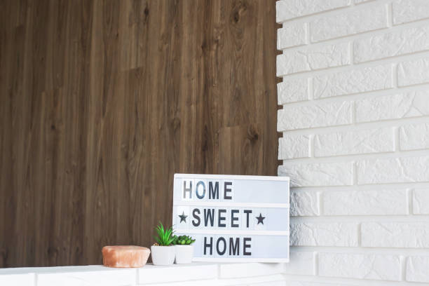 istock Home sweet home - it is written on a decorative frame with illumination in the interior between a white brick wall and a brown wooden one next to succulents and a pink candlestick. Copyspace 1047631018