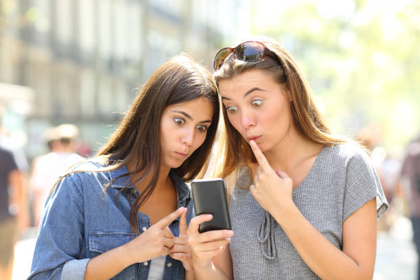 istock Perplexed girls checking smart phone outdoors 1047631030