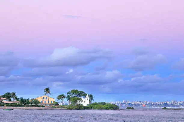 Sunset near Penha church on the isle of Itaparica, Bahia, Brazil; in the background the skyline of Salvador