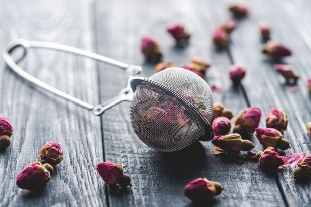 istock dried rose buds tea and tea strainer on wooden table 1047640324