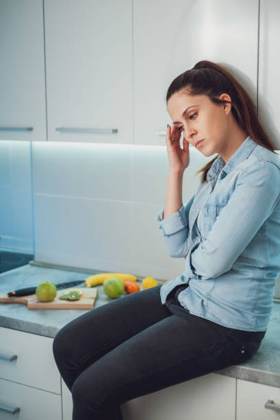 istock Sad girl having headache and sitting on kitchen countertop 1047640600