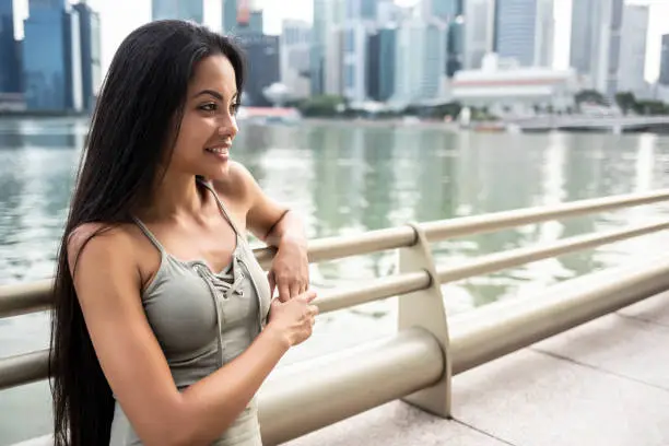 Smiling young woman standing in front of skyscrapers, leaning on a fence.