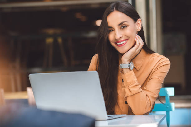 istock smiling young female freelancer looking at camera while working on laptop at table in cafe at urban street 1047648626