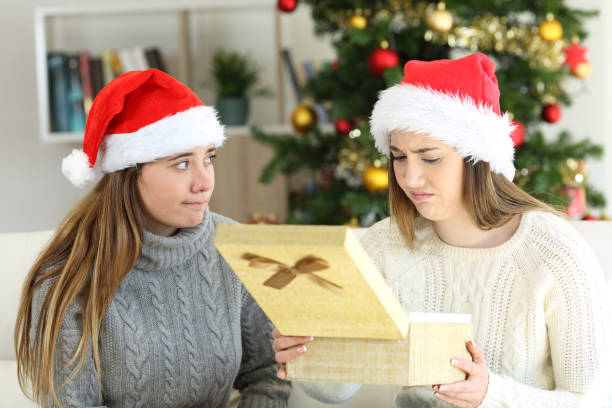 Disappointed woman receiving a gift in christmas Disappointed woman receiving a gift from a frustrated friend in christmas at home unliked stock pictures, royalty-free photos & images