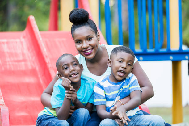 African-American woman with sons on playground A mid adult African-American woman in her 30s sitting on a playground slide with her two son, 4 and 5 years old. The older boy on the left. They are smiling at the camera. playground photos stock pictures, royalty-free photos & images