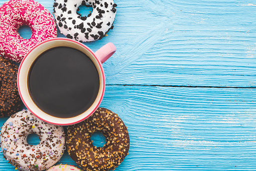 Coffee cup and colorful donuts on wooden blue background with space on text. Top View