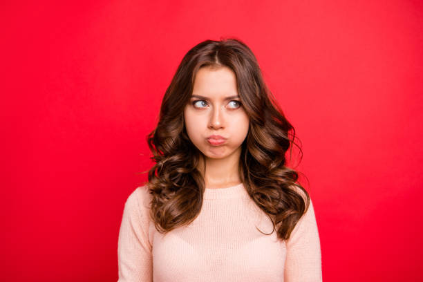 concepto de mal humor. retrato de dama adorable, fascinante, lindo, dulce mirada a un lado con las mejillas de aire grande, peinado moderno aislado sobre fondo rojo vivo de cerca - one cross fotografías e imágenes de stock