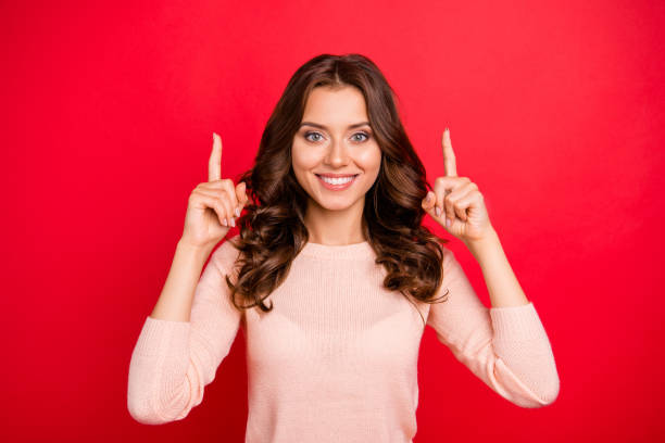 istock Stylish, curly lady with modern hairstyle indicate up forefinger on two hands isolated on vivid red background make big hollywood smile 1047661906