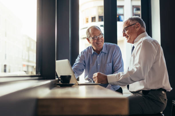 Business men working together in modern cafe Two senior business men working together in modern cafe. Business partners sitting near window with laptop on table at restaurant. working seniors stock pictures, royalty-free photos & images