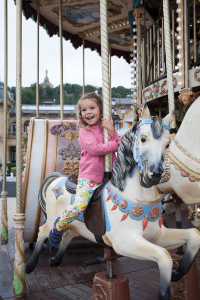 Adorable little toddler girl riding on animal on roundabout carousel in amusement park. Happy healthy baby child having fun outdoors on sunny day. Family weedend or vacations.