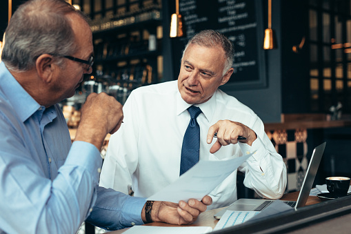 Business people discussing business reports while sitting at cafe. Two business partners reviewing documents at a coffee shop.