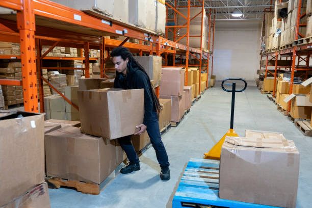 un addetto al magazzino che solleva una scatola utilizzando la tecnica corretta per il sollevamento sicuro - picking up safety working men foto e immagini stock