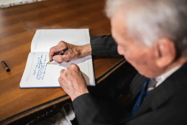 Older man writing something down on a piece of paper with pen