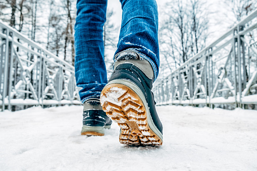 Man's legs in black with orange boots walking in the snow
