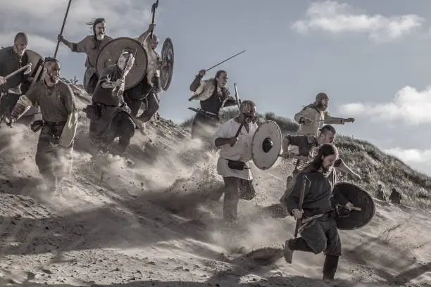 A hoard of Weapon wielding viking warriors on a sandy battlefield dune