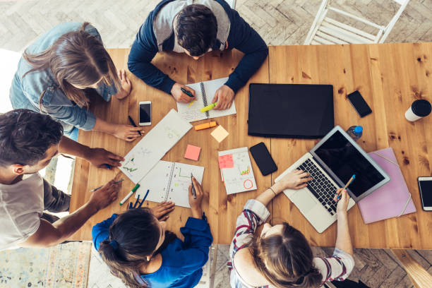 overhead view on business people around desk overhead view on young business people around wooden desk learning and development stock pictures, royalty-free photos & images