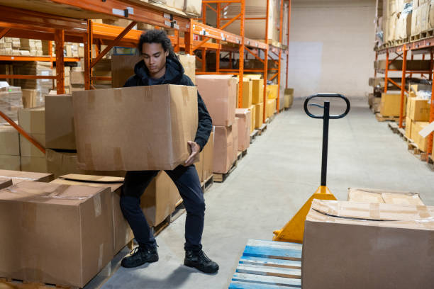 un addetto al magazzino che solleva una scatola utilizzando la tecnica corretta per il sollevamento sicuro - picking up safety working men foto e immagini stock