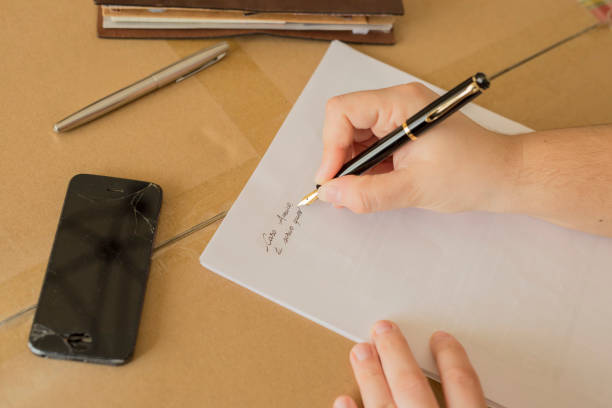 istock horizontal image of a hand writing a letter with broken phone on the desk 1047703240