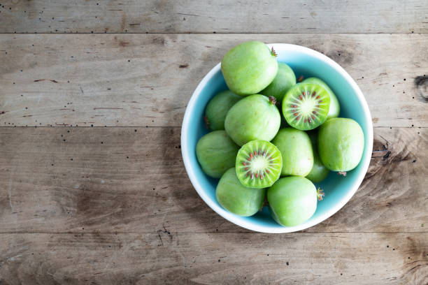 frutas de quivi résistentes ou quivi baga actinidia arguta na tigela de cerâmica na mesa da cozinha de madeira - actinidia - fotografias e filmes do acervo