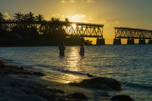This sunset view of two girls in the water at Bahia Honda State Park in the Florida Keys.  The Keys do not have a lot of sand beaches and this is arguably the most picturesque.  The bridge silhouette in the background is the abandoned railway that used to run the length of the keys all the way to Key West.  For sure a magical spot and scene.