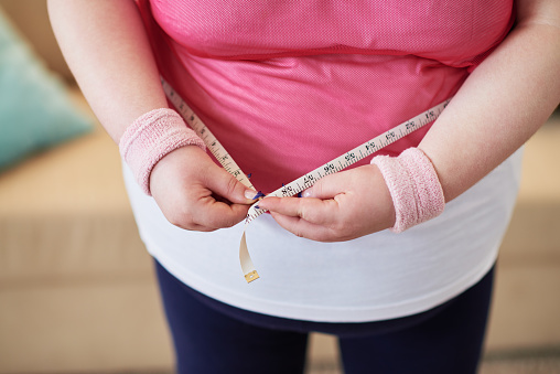 Close-up of overweight woman measuring her waist with tape measure