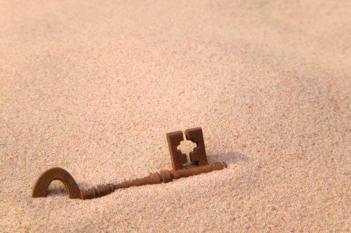 A rusty old key part buried in sand.