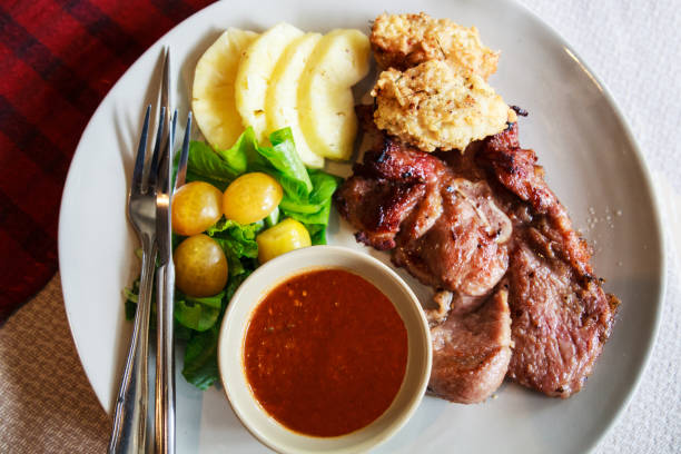 Thai Cuisine, Pork Steak with Deep Fried Sticky Rice dipped with traditional spicy red chili sauce and farm fresh vegetable tomato, Rocket Victoria and sweet pineapple in white dish table background.