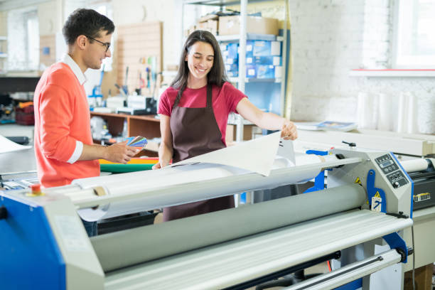 Picking out color for printing Cheerful excited beautiful lady in apron showing printed banner to manager who picking out color on swatch for printing printing press stock pictures, royalty-free photos & images