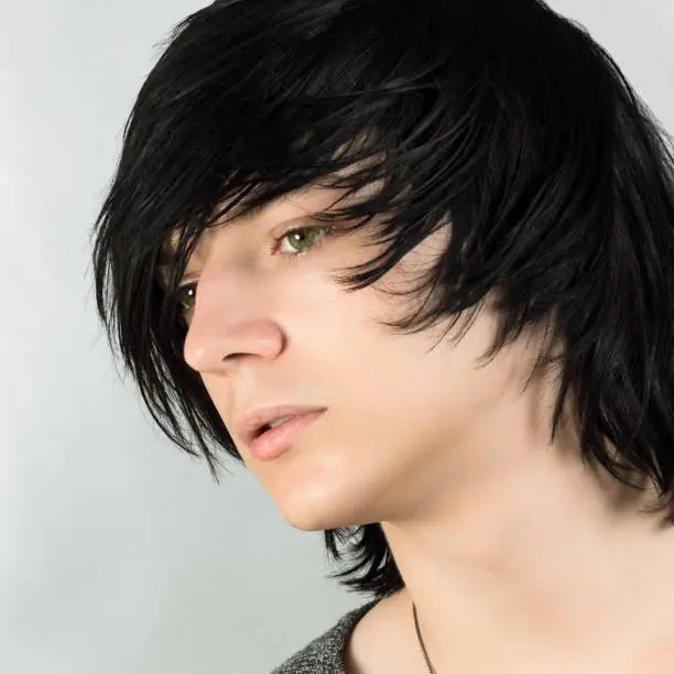 Close-up portrait of handsome teenage boy with black hair emo hairstyle on white background.