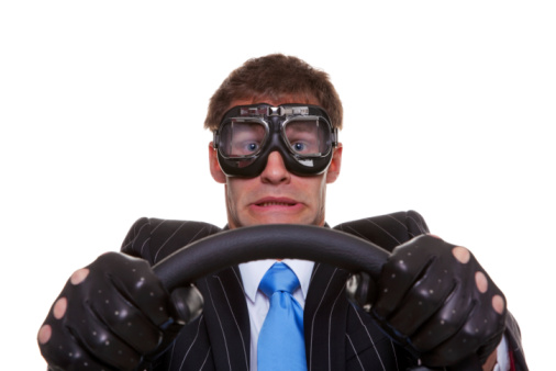 Businessman in driving gloves and goggles with a look of panic on his face, isolated on white background.