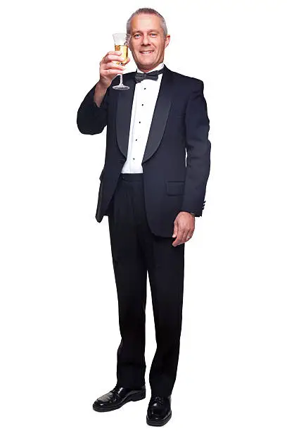 A mature male wearing a black tuxedo and bow tie raising a glass of champagne, isolated on a white background.
