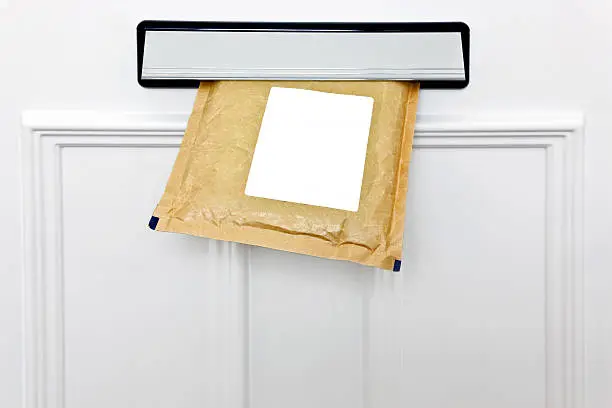A padded envelope in the letterbox of a white front door, blank label for you to add your own name and address.