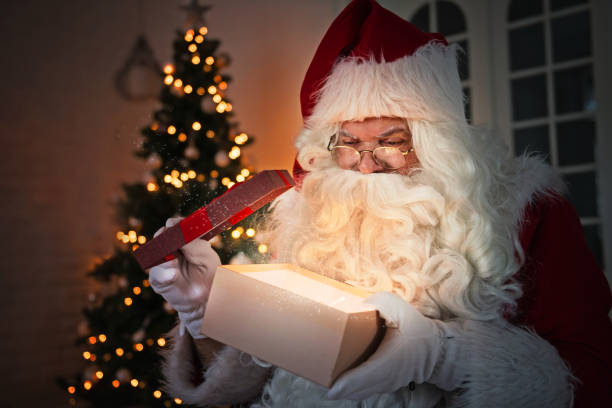 istock Santa Claus holding a present, Christmas tree in the background 1047749362