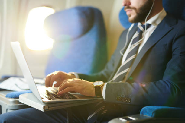 Businessman Using Laptop in Plane Closeup Mid section portrait of unrecognizable businessman typing on keyboard while using laptop during first class flight in plane, copy space business travel stock pictures, royalty-free photos & images