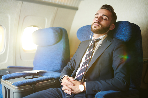 Portrait of handsome bearded businessman wearing earphones sleeping blissfully while enjoying first class flight in plane, copy space