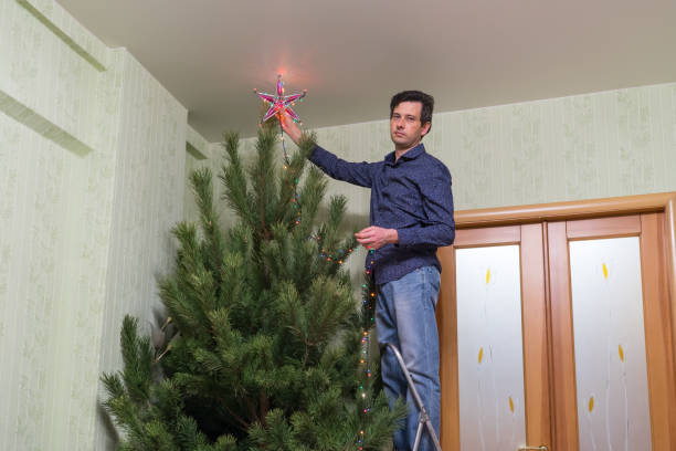 il bel uomo di mezza età decora un albero di natale con una stella - new year wall door decoration foto e immagini stock