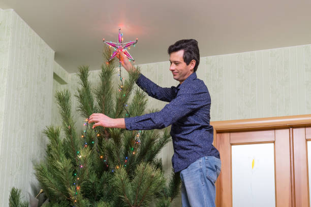 il bel uomo di mezza età decora un albero di natale con una stella - new year wall door decoration foto e immagini stock