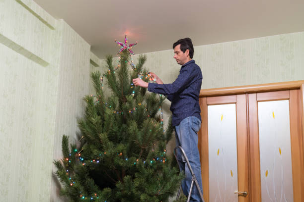 il bel uomo di mezza età decora un albero di natale con una stella - new year wall door decoration foto e immagini stock