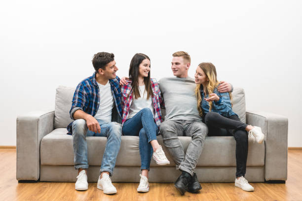 istock The four happy friends sit on the sofa on a white wall background 1047775360