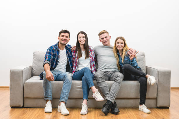 istock The four happy friends sit on the sofa on a white wall background 1047775370