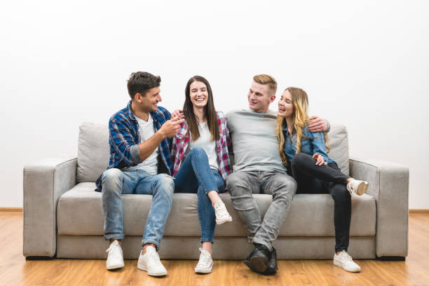 istock The four happy friends sit on the sofa on a white wall background 1047775402