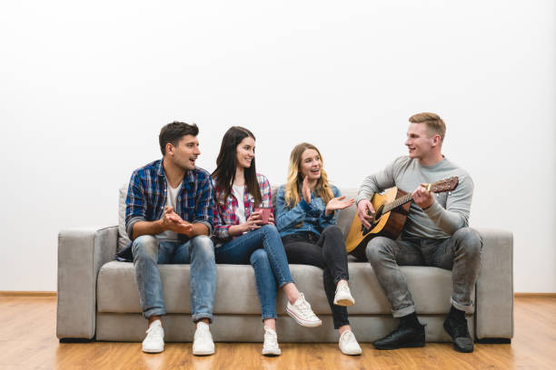 istock The four friends with a guitar sit on the sofa on the white wall background 1047778748