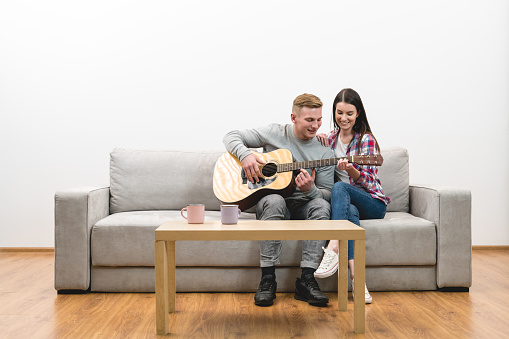The couple sit on the sofa and play the guitar on the white wall background